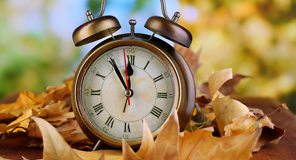 Old clock on autumn leaves on wooden table on natural background